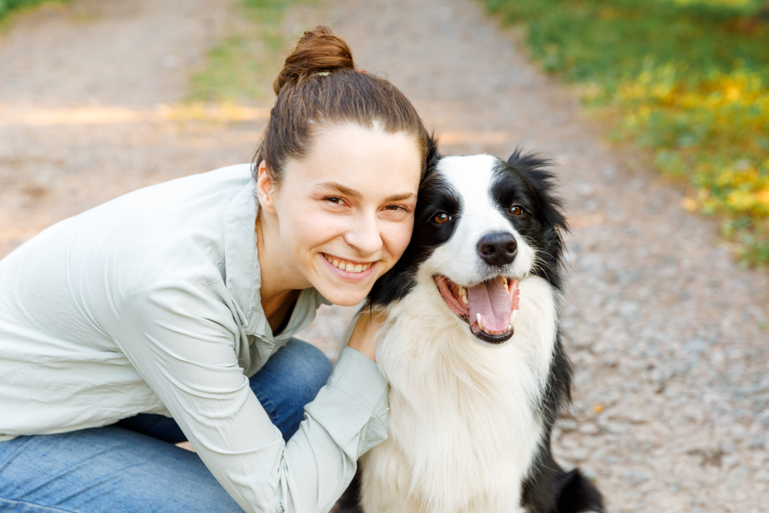 Smiling young attractive woman playing with cute puppy dog border collie on summer outdoor background. Girl holding embracing hugging dog friend. Pet care and animals concept.